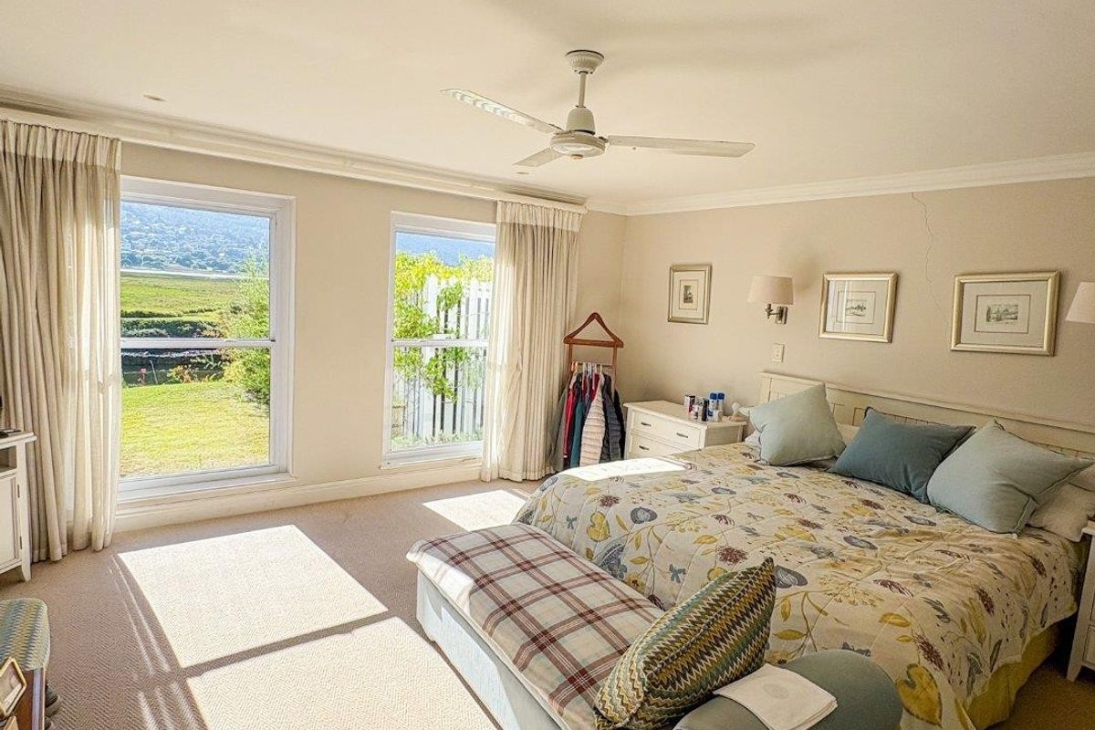 Spacious bedroom featuring carpet flooring, a ceiling fan, and large windows with natural light and garden views.