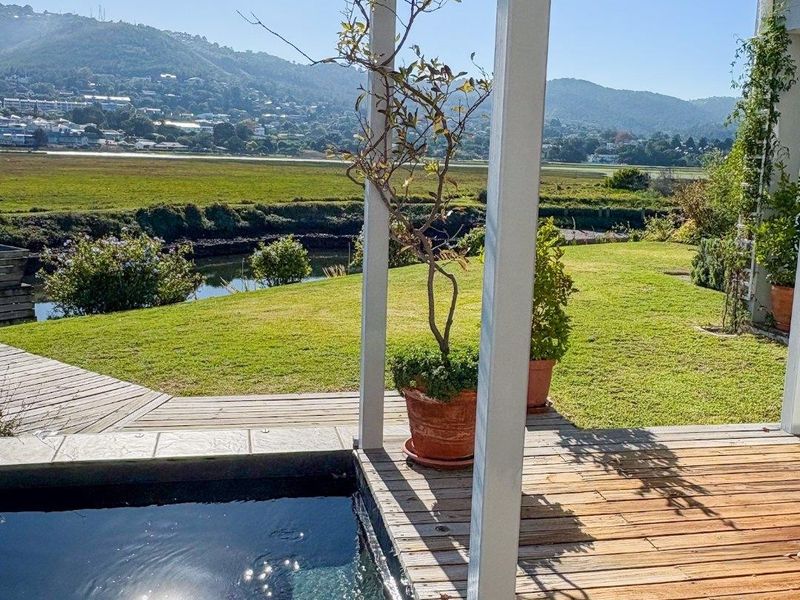 A serene outdoor pool area featuring timber decking, a plunge pool, and a covered patio overlooking a lush garden and scenic landscape.