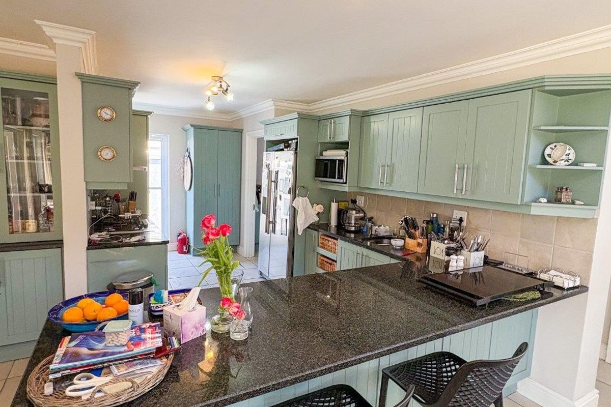 A well-maintained kitchen featuring sage green cabinetry, dark granite countertops, a breakfast bar, and tiled flooring with integrated lighting.
