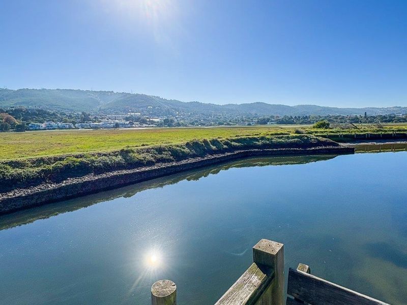 A scenic view overlooking a tranquil river and expansive green landscape, captured from a wooden deck structure.