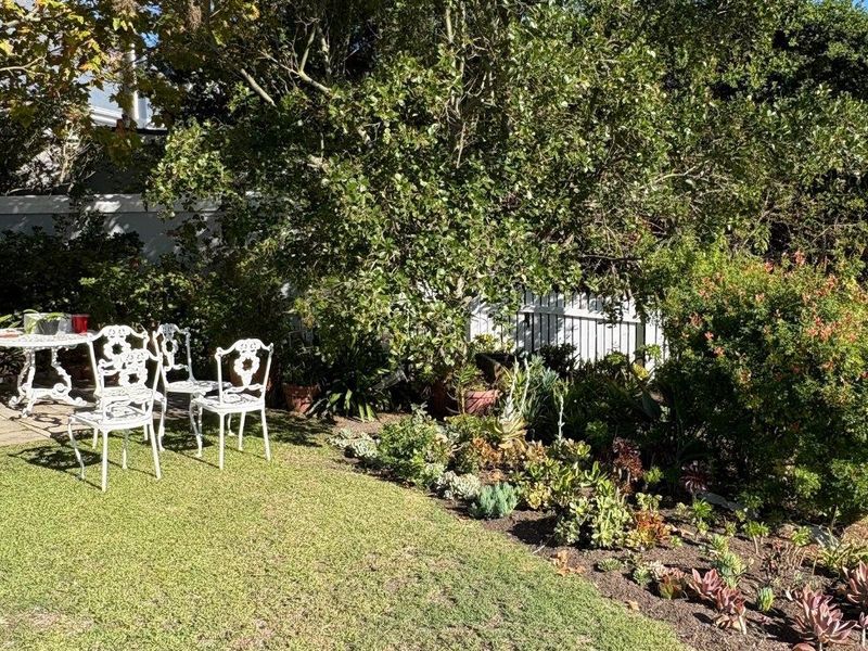 A well-maintained private garden featuring a lush lawn, mature trees, and a landscaped succulent bed bordered by a white picket fence.