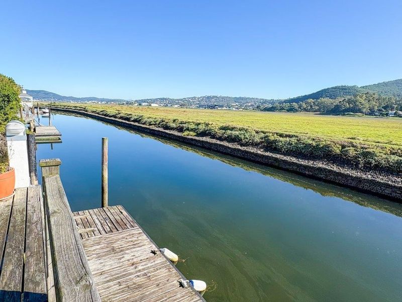 Scenic view of a tranquil waterway and marshland, featuring a private wooden jetty and timber railing.
