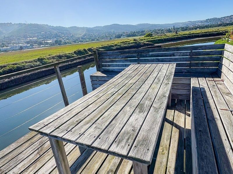 An outdoor timber deck featuring built-in bench seating and a table, offering scenic views over the adjacent waterway and landscape.