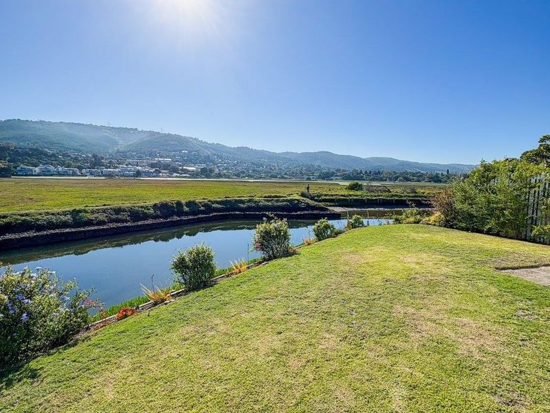 A scenic outdoor view featuring a well-maintained lawn overlooking a tranquil waterway with distant mountain vistas.