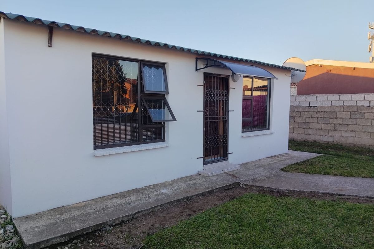 Rear exterior view of the house featuring a concrete walkway, security gates on windows and doors, and a corrugated metal roof.