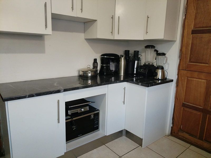 A functional scullery area featuring white cabinetry, dark laminate countertops, and tiled flooring, providing additional storage and prep space.