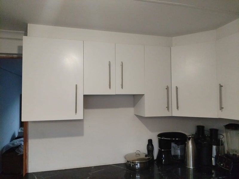 A functional kitchen area featuring clean white cabinetry with modern stainless steel handles and a dark stone countertop.