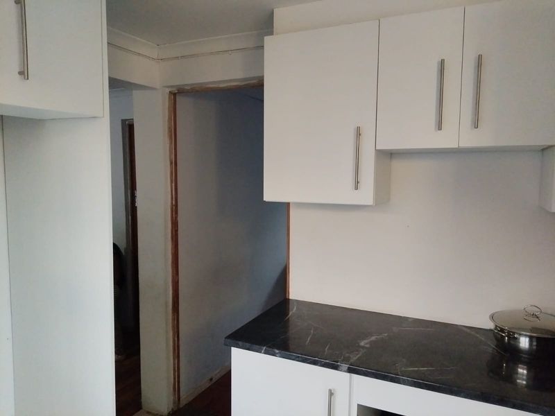 A kitchen area featuring white built-in cabinetry and dark marble-effect countertops, currently showing unfinished door frames and wall edges.