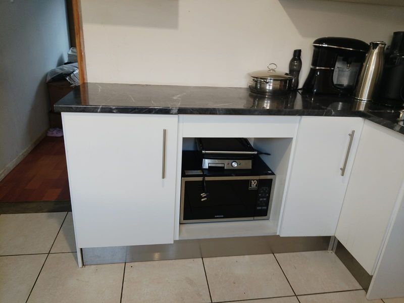 A modern kitchen section featuring white cabinetry, a dark marble-effect laminate countertop, and neutral floor tiles.