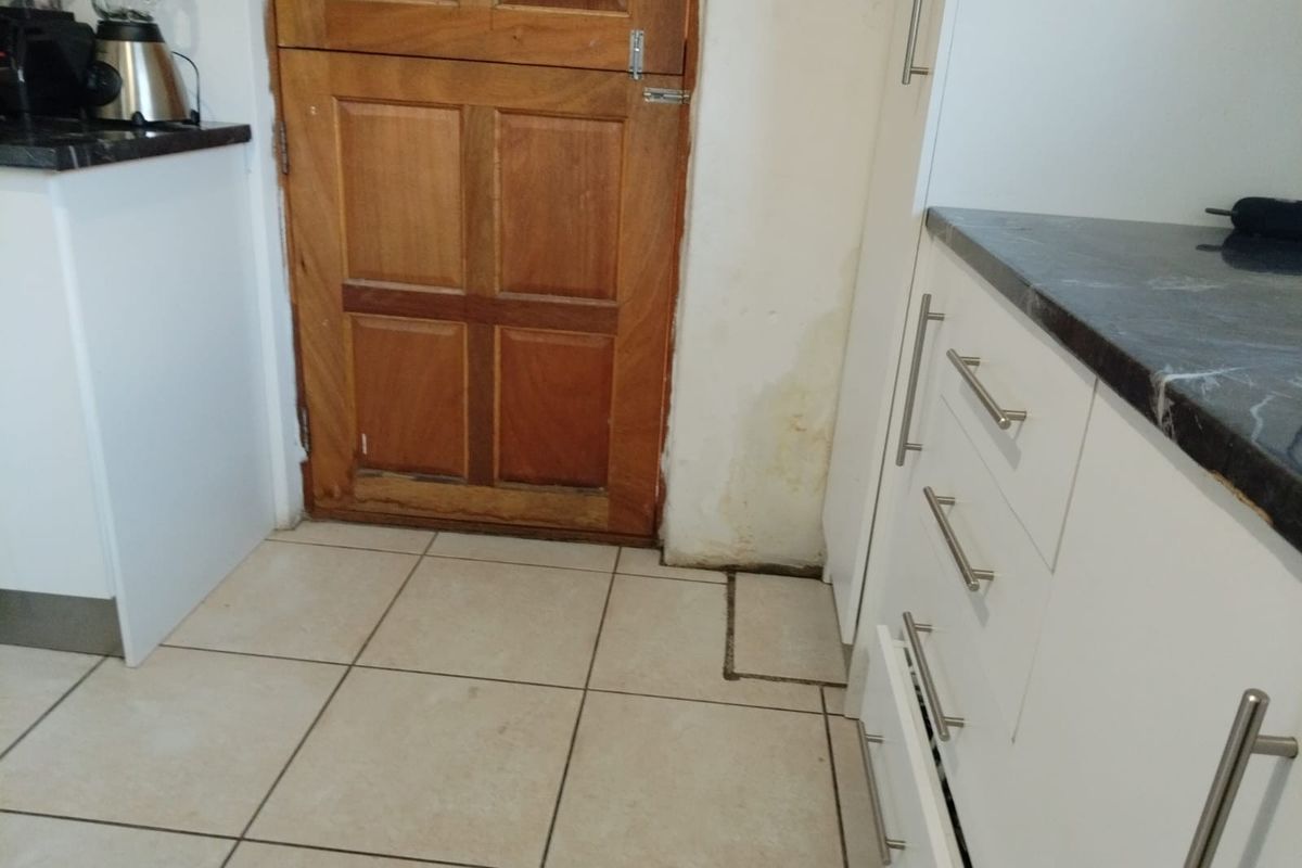 Kitchen area featuring white cabinetry, dark countertops, and ceramic flooring, with visible water damage on the wall and door frame requiring attention.