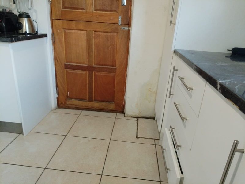 Kitchen area featuring white cabinetry, dark countertops, and ceramic flooring, with visible water damage on the wall and door frame requiring attention.