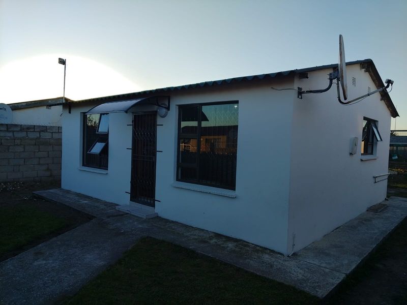 A view of the rear exterior of the house featuring white painted walls, aluminium window frames, and a concrete pathway.
