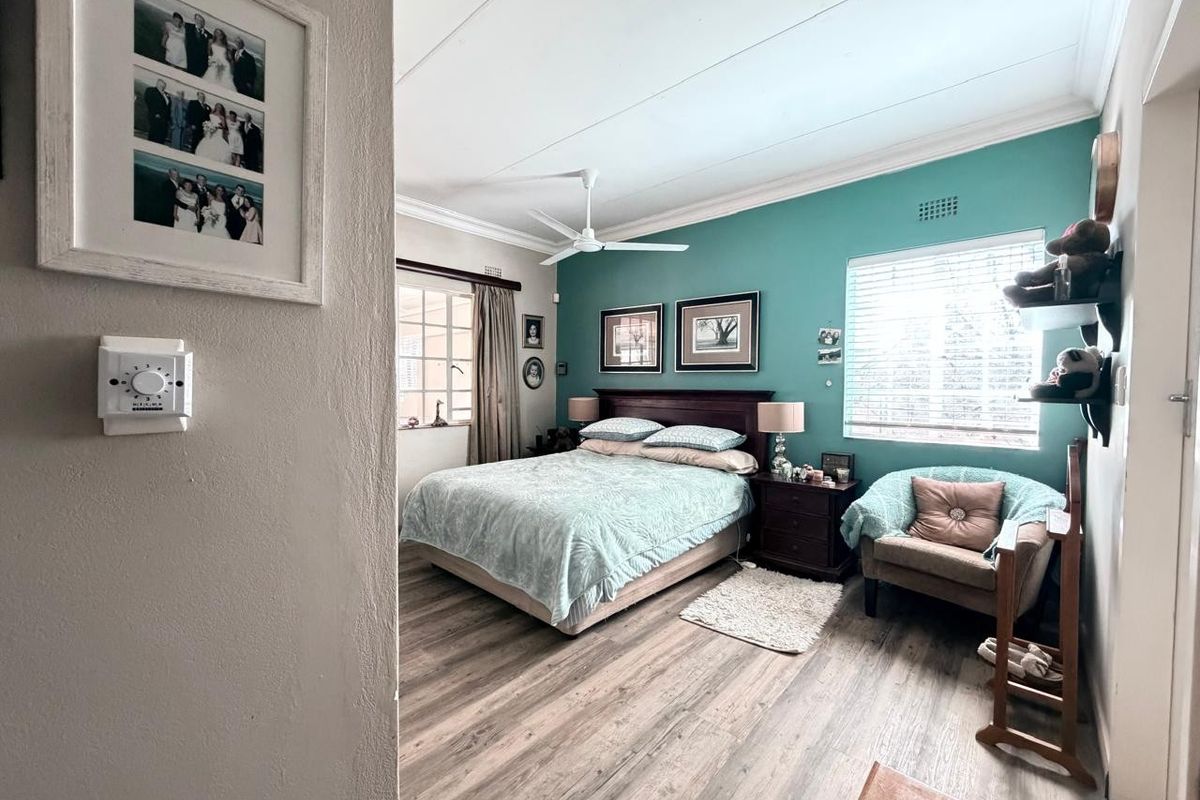 A well-maintained bedroom featuring laminate flooring, a ceiling fan, and a feature wall with window blinds.