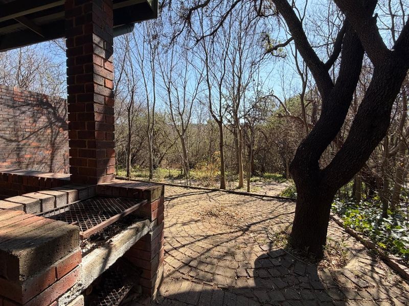 A rustic outdoor patio area featuring a built-in brick braai, brick paving, and a natural wooded outlook.