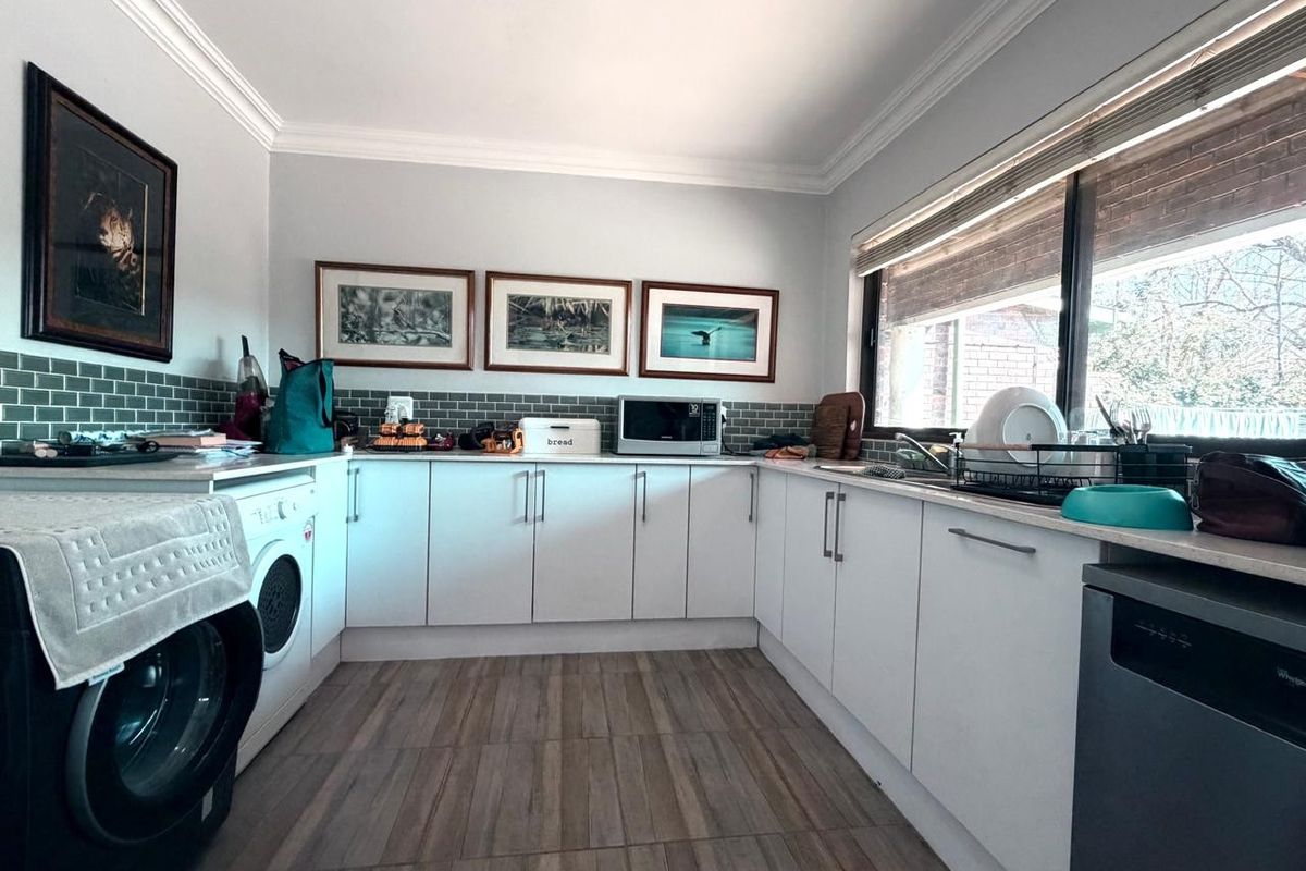 A functional kitchen featuring white cabinetry, subway tile backsplash, wood-look tiled flooring, and ample counter space with integrated sink and appliance housing.