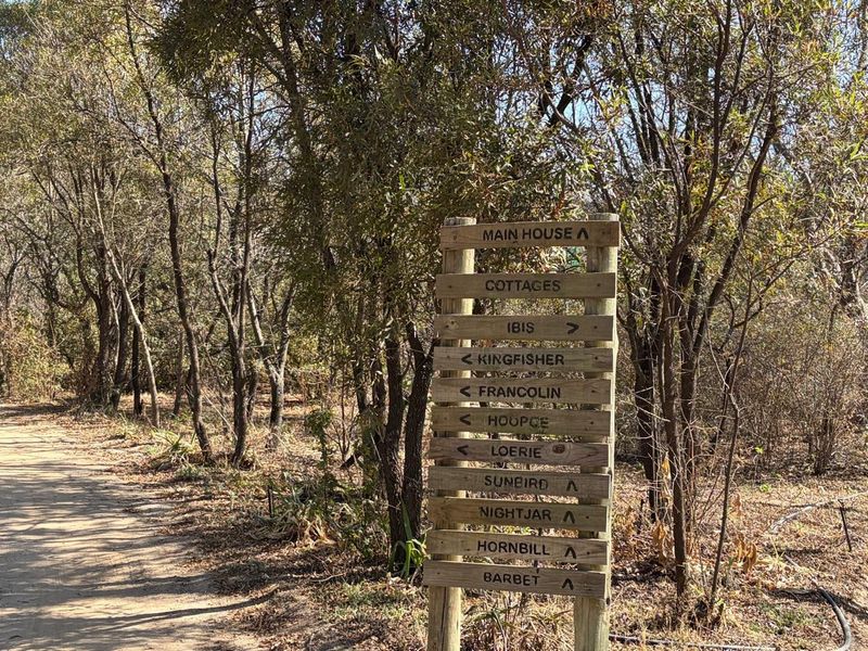 A wooden directional signpost located on a farm property, indicating the paths to the main house and various cottages.