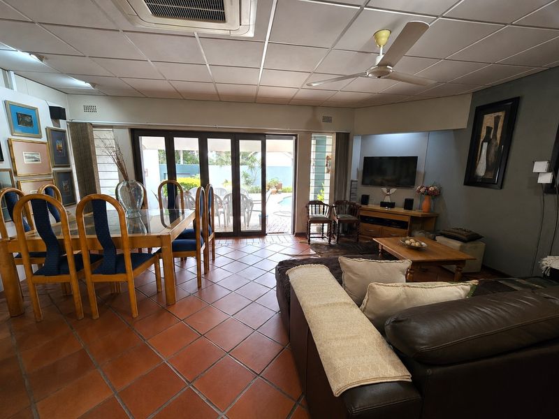 Spacious open-plan living and dining area featuring terracotta floor tiles, a ceiling fan, and large sliding glass doors providing access to the outdoor patio.