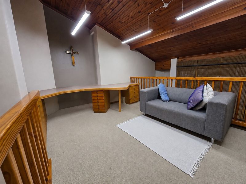 A loft-style office space featuring a built-in desk, timber-clad vaulted ceiling, and a wooden balustrade overlooking the lower level.