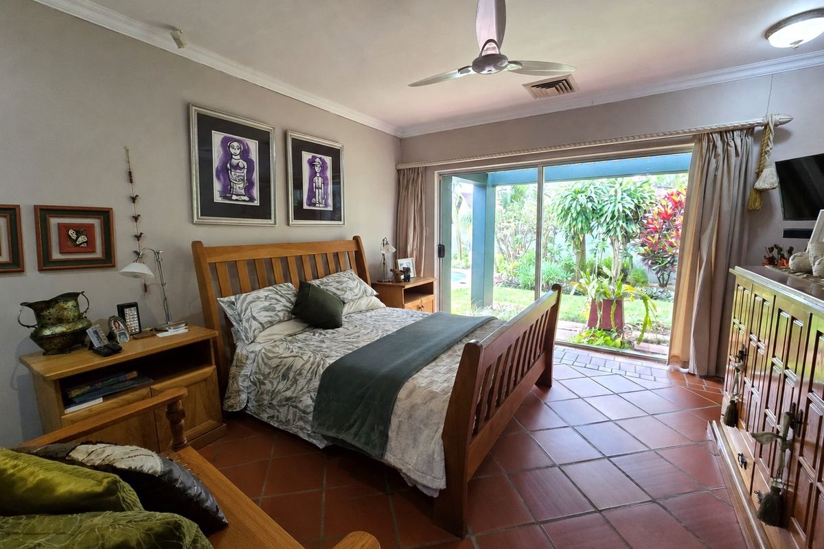 Spacious bedroom featuring terracotta floor tiles, a ceiling fan, and large sliding glass doors providing direct access to the garden area.