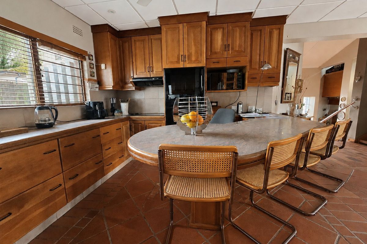 A spacious kitchen featuring warm wooden cabinetry, a large central island with a laminate countertop, and traditional terracotta tiled flooring.