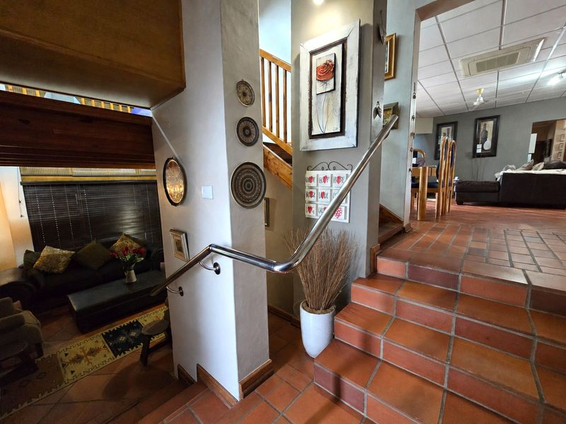 A split-level hallway featuring terracotta tile flooring, a stainless steel handrail, and a wooden staircase leading to upper levels.