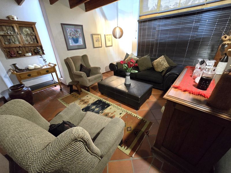 A cozy living room featuring exposed timber ceiling beams, terracotta floor tiles, and a large window with venetian blinds.
