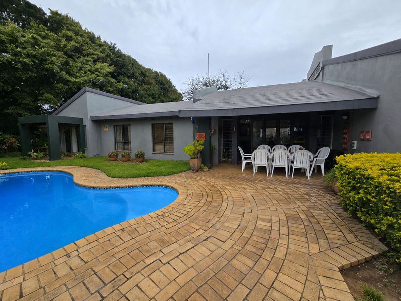 Rear exterior view featuring a swimming pool, a circular paved patio area, and a grey-painted house facade with a tiled roof.