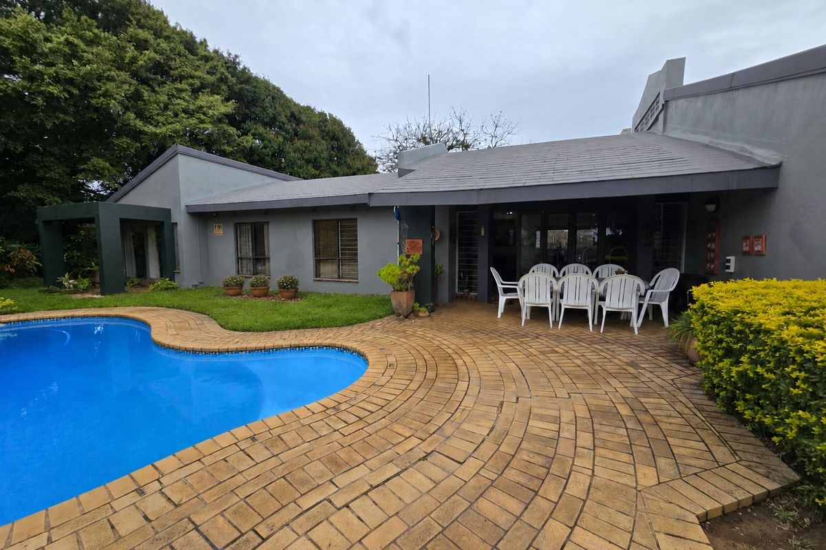 Rear exterior view featuring a swimming pool, a circular paved patio area, and a grey-painted house facade with a tiled roof.