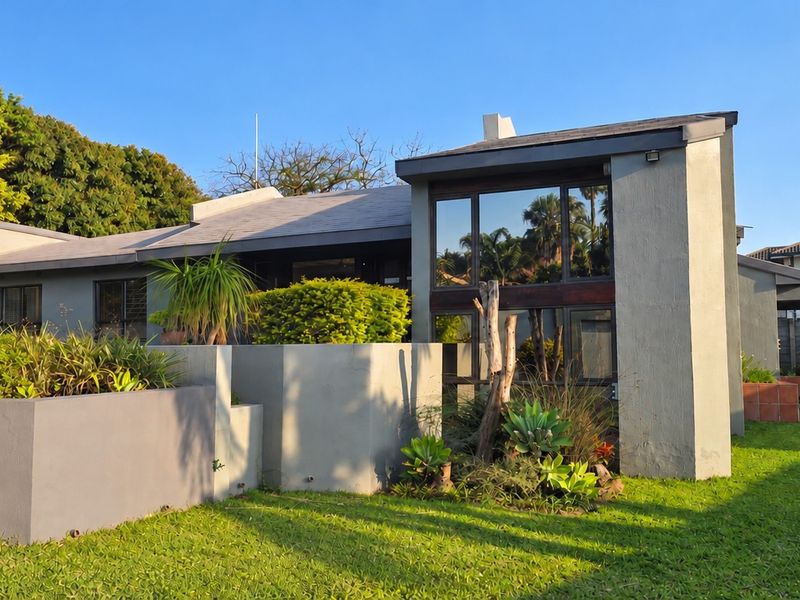A modern residential exterior featuring concrete planter boxes, large glass windows, and a well-maintained garden area.