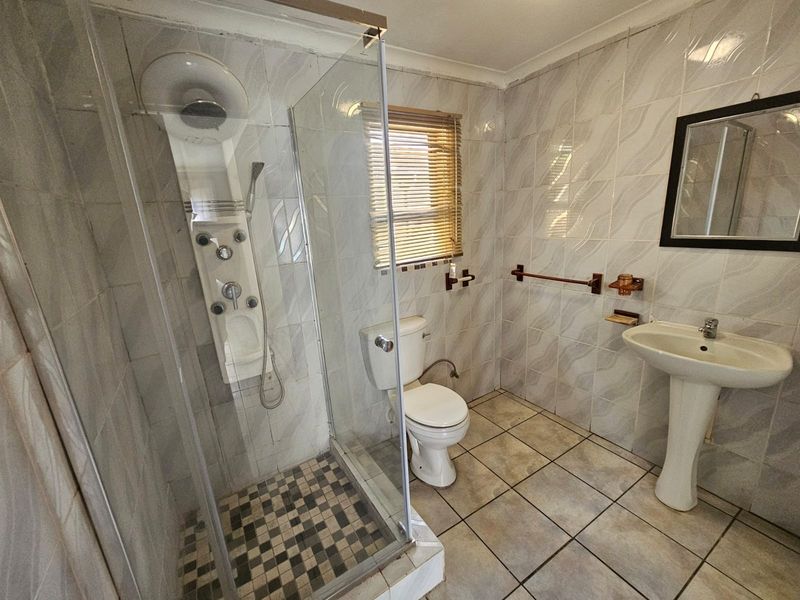 A functional bathroom featuring a glass shower enclosure with a shower panel, pedestal basin, and fully tiled walls and flooring.