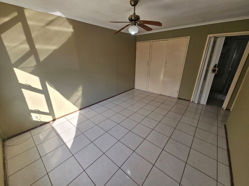 An empty bedroom featuring tiled flooring, a ceiling fan, and built-in cupboards, offering a blank canvas for personalization.