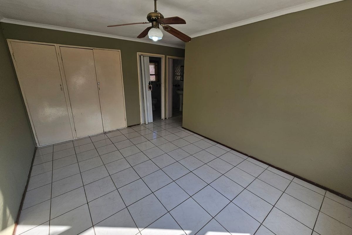 An empty bedroom featuring tiled flooring, built-in cupboards, and a ceiling fan, with direct access to an en-suite bathroom.