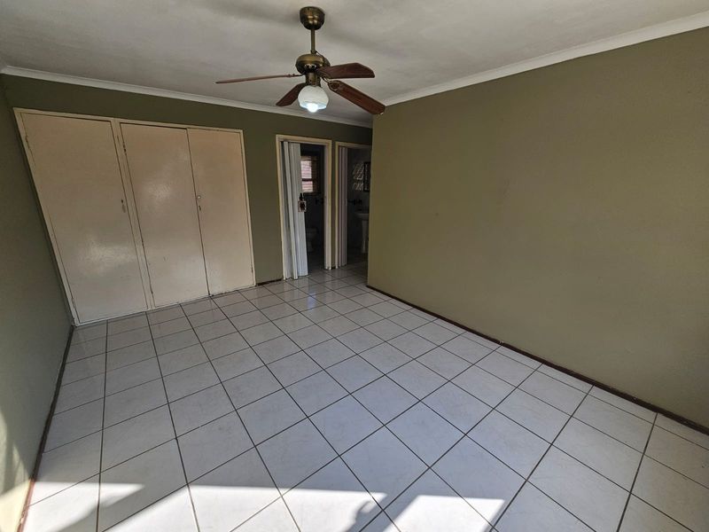 An empty bedroom featuring tiled flooring, built-in cupboards, and a ceiling fan, with direct access to an en-suite bathroom.