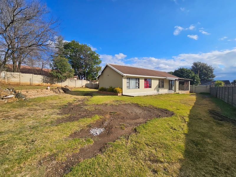Rear view of the house featuring a tiled roof, concrete patio, and a spacious garden enclosed by precast concrete boundary walls.