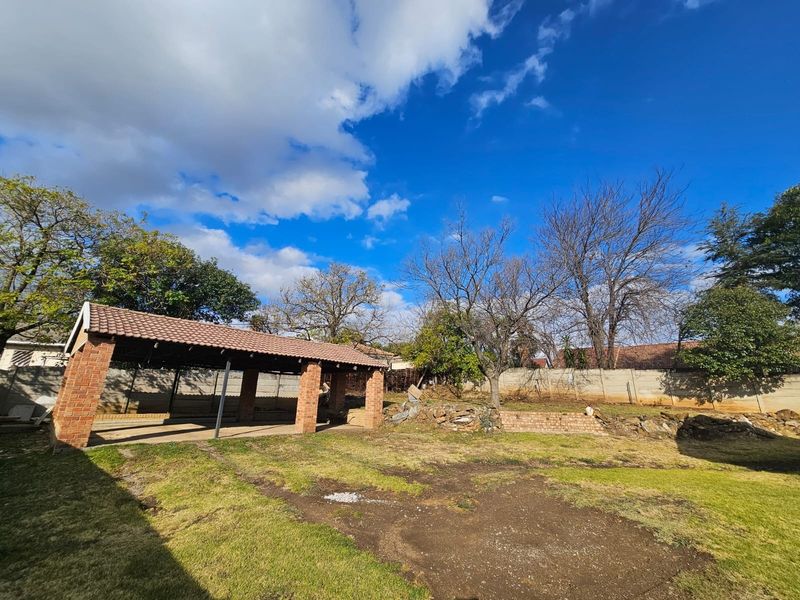 Spacious rear garden featuring a covered brick patio structure, concrete boundary walls, and established landscaping with potential for further development.