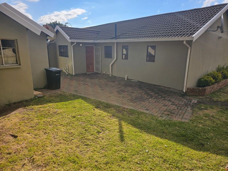 Rear view of the house featuring a paved patio area, tiled roof, and established garden space.