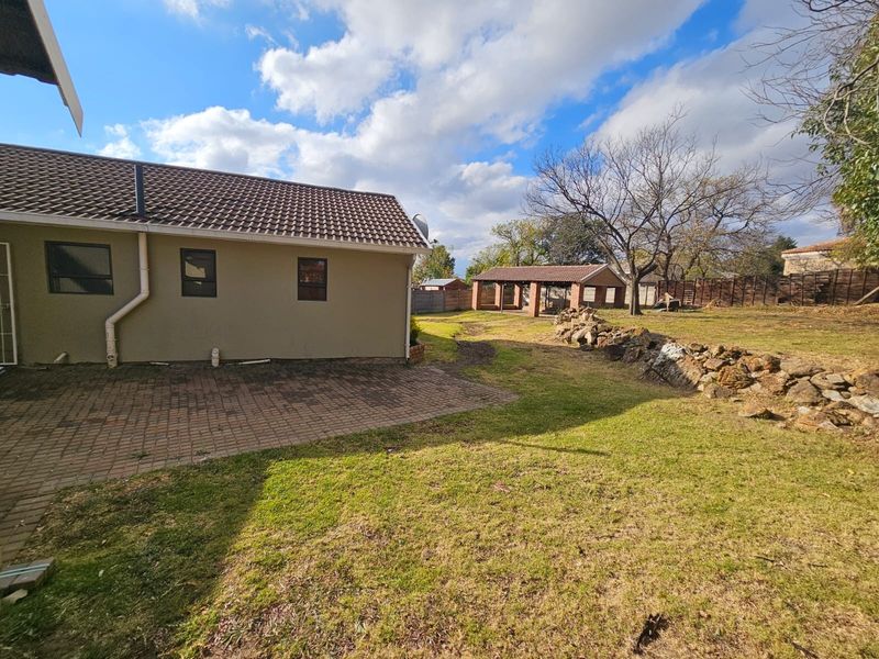 Spacious rear garden featuring a paved patio area, stone retaining wall, and a detached brick outbuilding under a tiled roof.