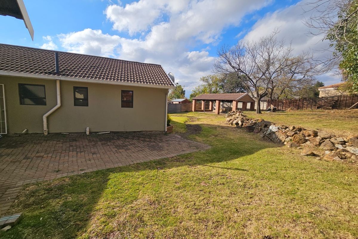 Spacious rear garden featuring a paved patio area, stone retaining wall, and a detached brick outbuilding under a tiled roof.
