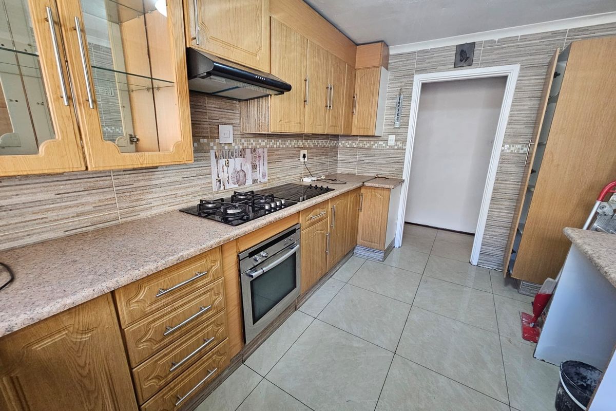 A functional kitchen featuring wooden cabinetry, built-in oven and gas hob, tiled backsplash, and neutral floor tiles, offering a solid foundation for modern updates.