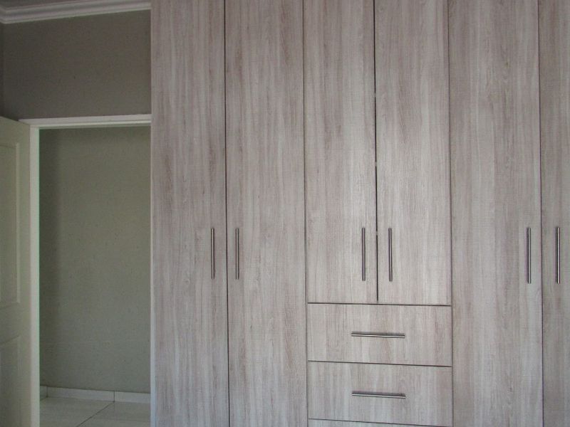 A bedroom featuring modern light wood-grain built-in cupboards, tiled flooring, and neutral wall finishes.