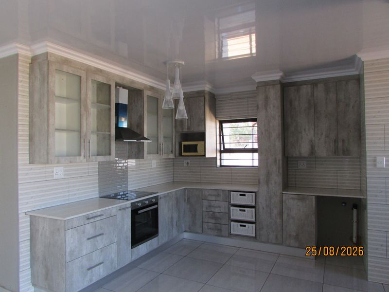 Modern kitchen featuring grey wood-look cabinetry, integrated appliances including an oven and hob, tiled splashbacks, and a high-gloss ceiling finish.