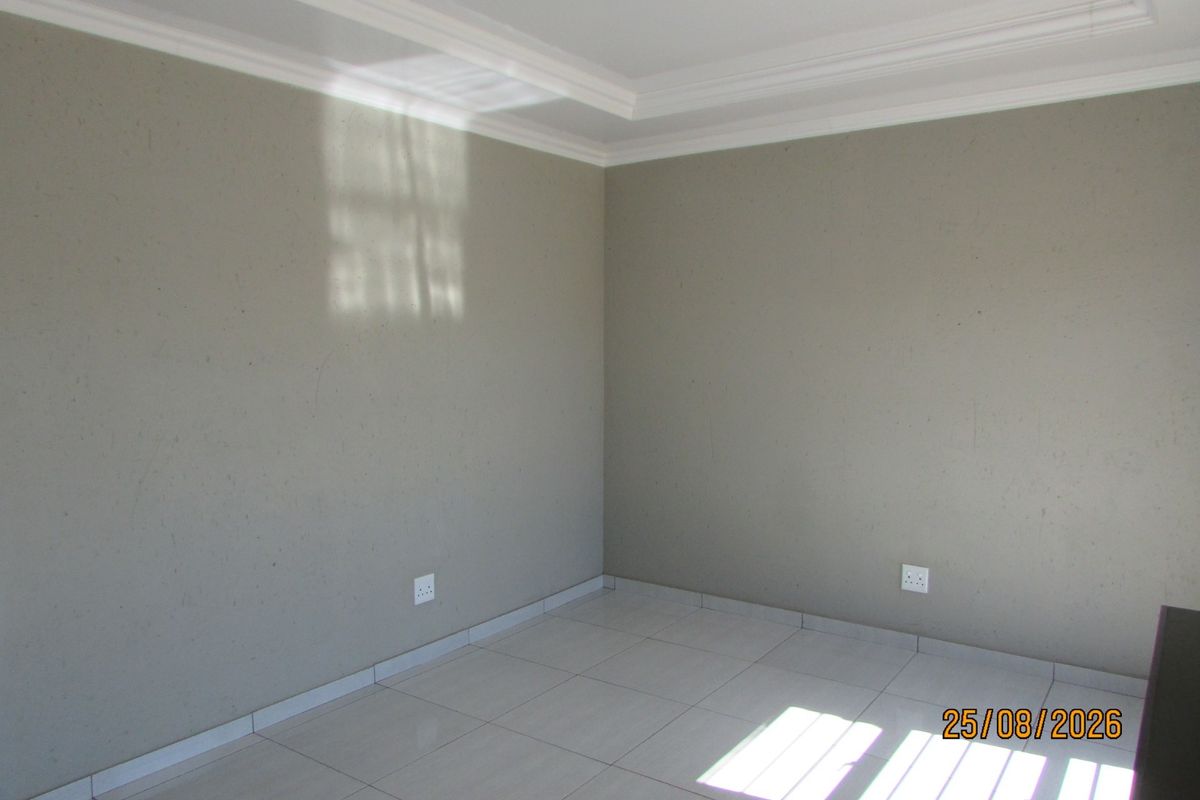A clean, empty bedroom featuring neutral grey walls, tiled flooring, and decorative ceiling cornicing, providing a blank canvas for personalization.
