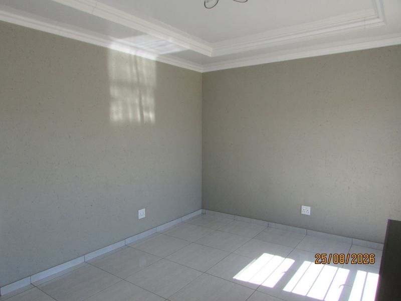 A clean, empty bedroom featuring neutral grey walls, tiled flooring, and decorative ceiling cornicing, providing a blank canvas for personalization.