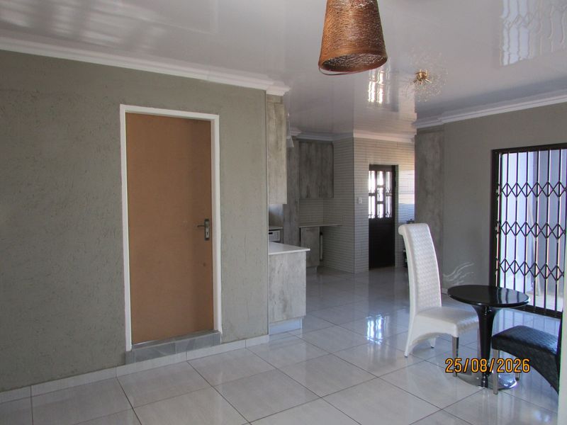 Open plan living and kitchen area featuring tiled flooring, glossy ceiling, and a security gate, offering a functional layout with potential for modern updates.