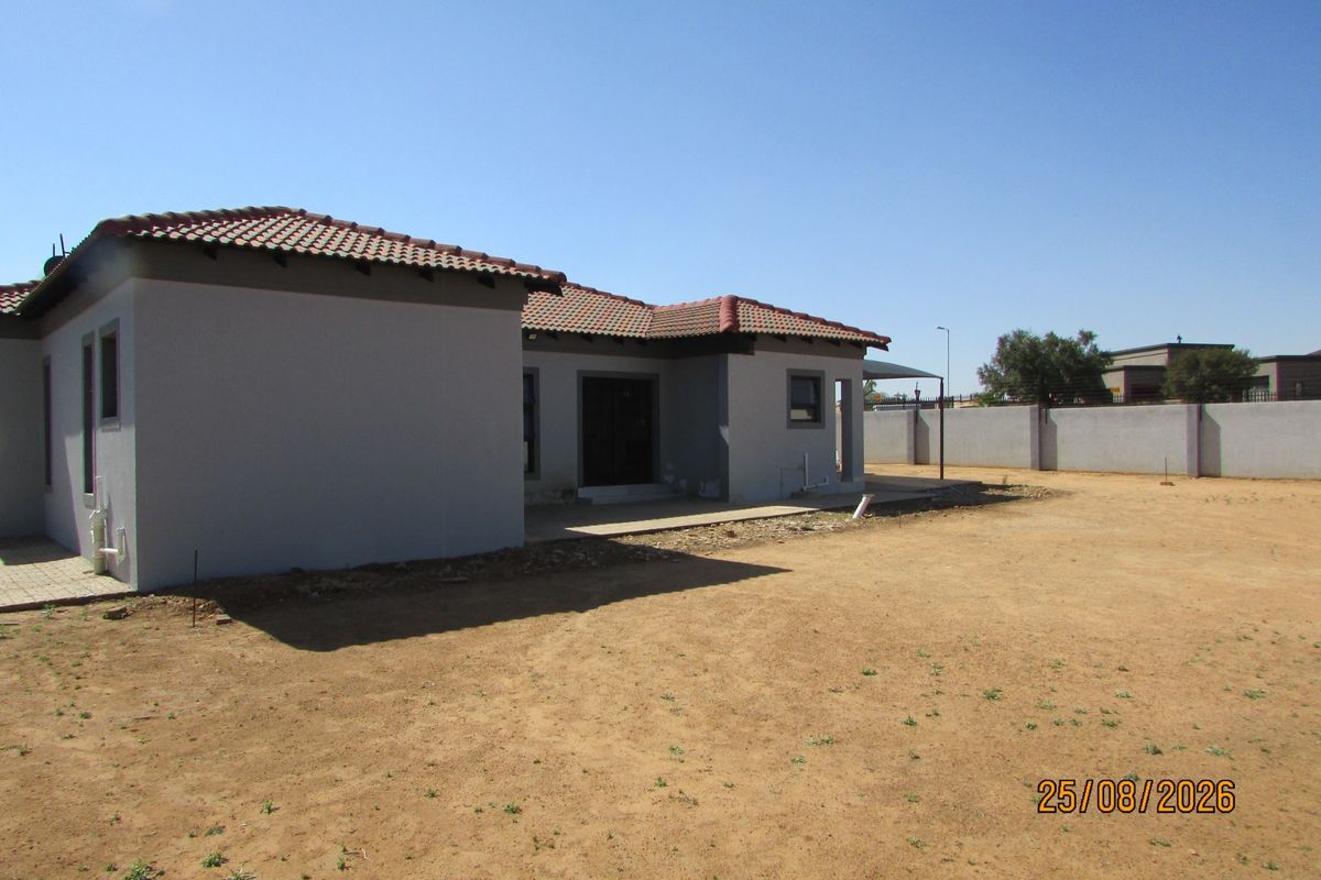 Rear view of the house featuring a tiled roof, concrete patio area, and a large, undeveloped garden space enclosed by a perimeter wall.