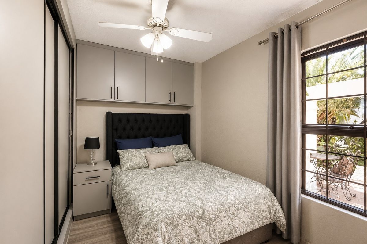 A well-maintained bedroom featuring built-in cupboards, a ceiling fan, and a sliding door wardrobe, offering efficient storage and comfortable living space.