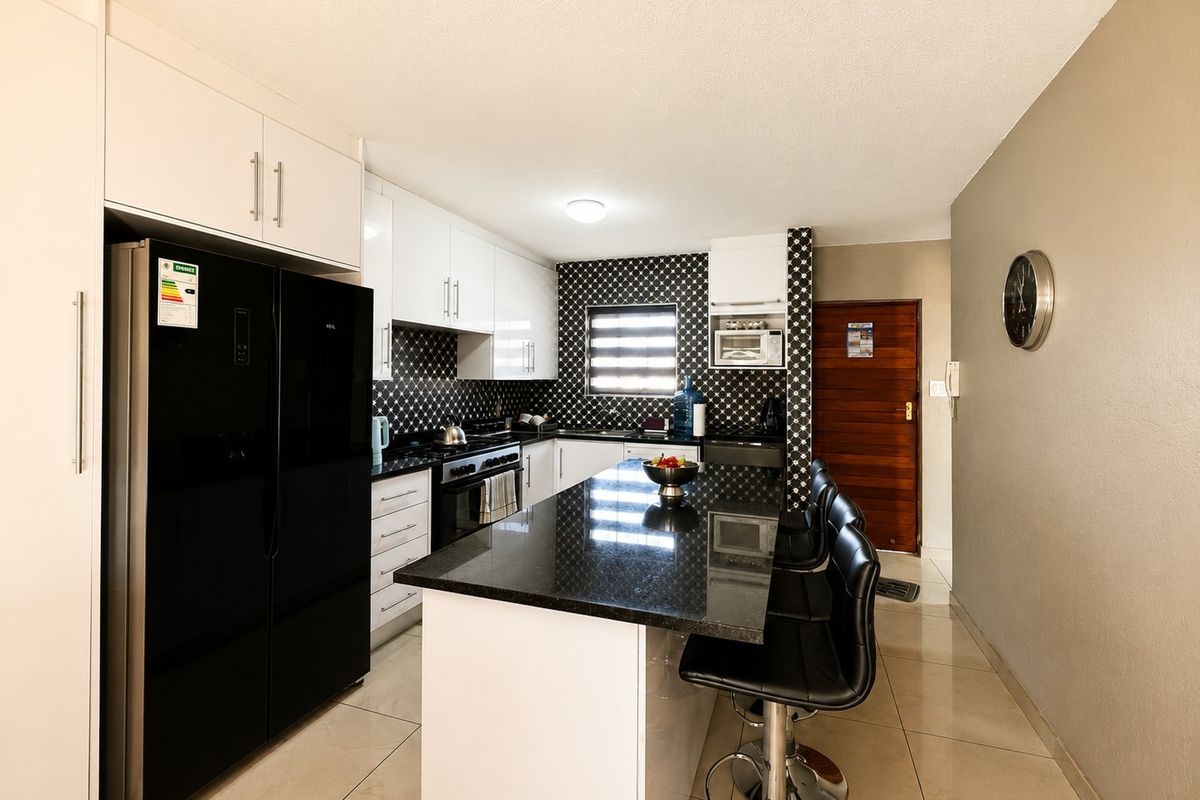 Modern kitchen featuring white cabinetry, black granite countertops, a central island with breakfast bar seating, and a striking patterned backsplash.
