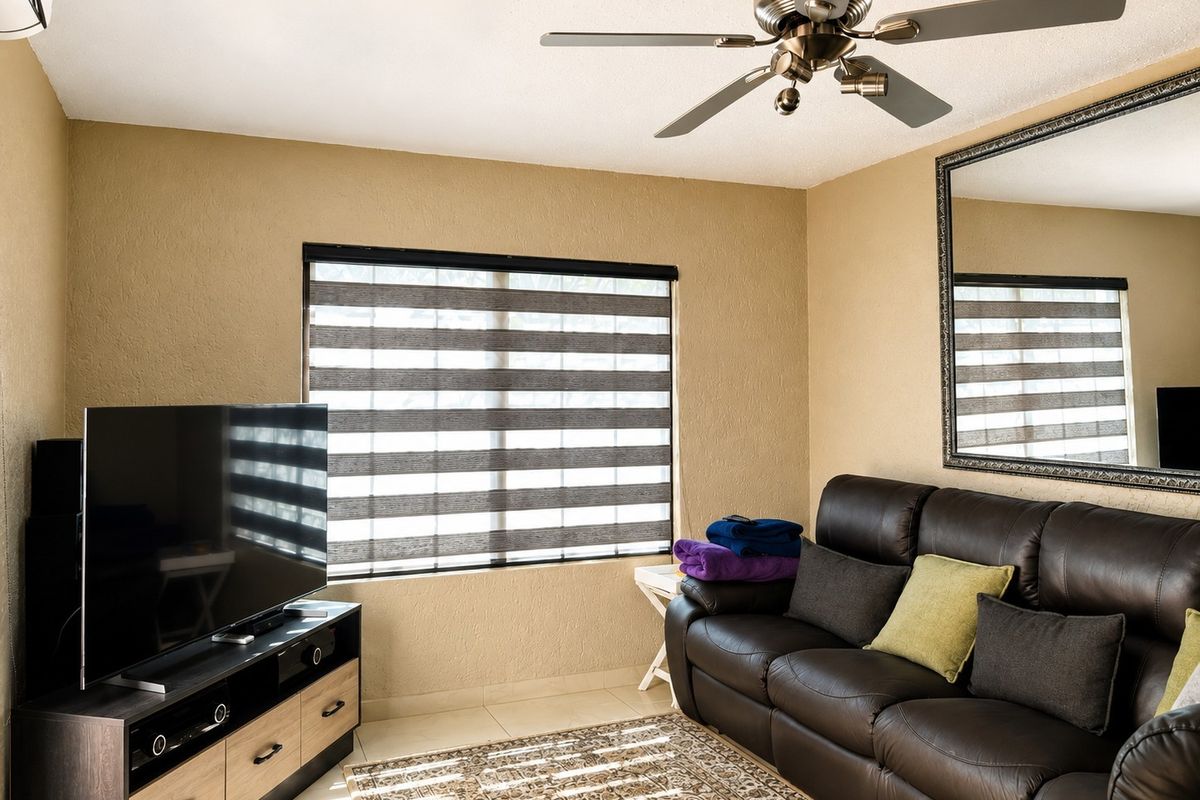 A living room featuring a ceiling fan, tiled flooring, and modern roller blinds, providing a functional and comfortable space.