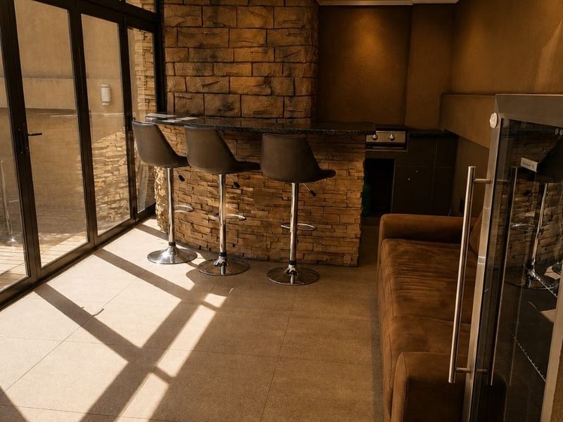 A modern indoor bar area featuring a stone-clad counter with granite top, recessed lighting, and large aluminium sliding doors opening to the exterior.