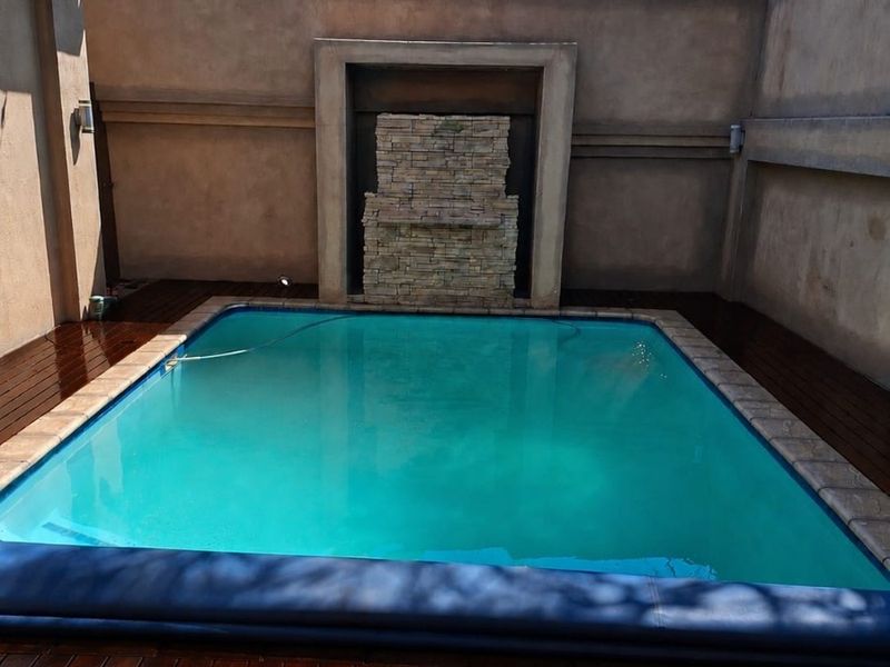 A private pool area featuring a stone water feature, surrounded by well-maintained timber decking and high perimeter walls with electric fencing.